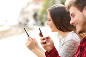 Pareja mirando los teléfonos, chica y chico enviando mensajes de texto, pareja sosteniendo los teléfonos