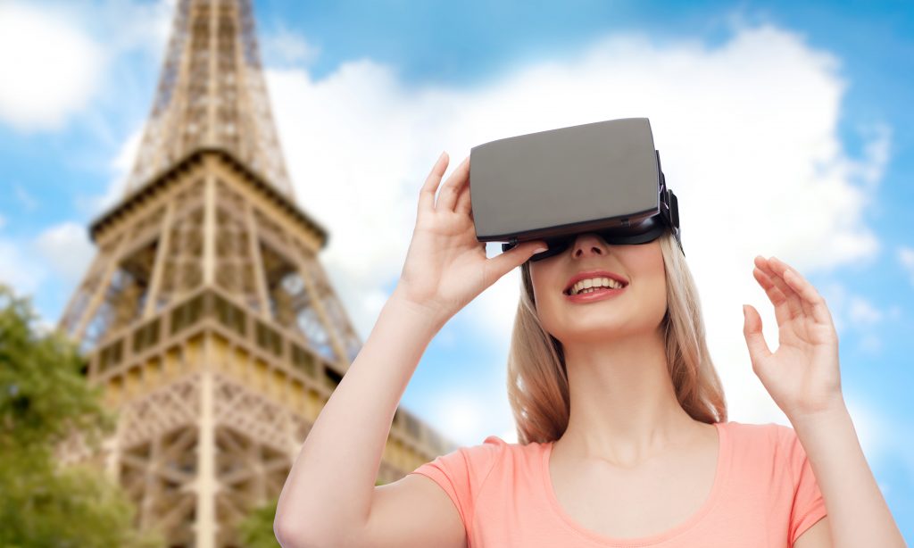 technology, virtual reality, entertainment, travel and people concept - happy young woman with virtual reality headset or 3d glasses over Eiffel tower background