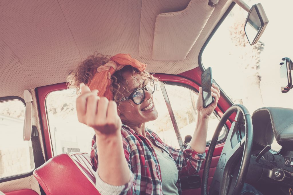 Adult female listening to music inside a red vintage car, curly haired woman listening to music inside a car, woman listening to music from her phone inside a car 