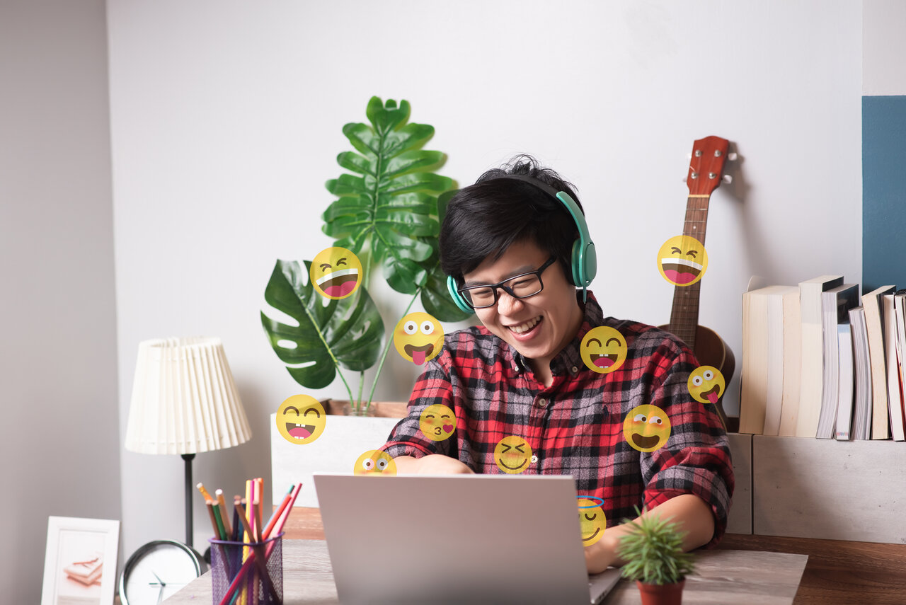 Young adult Asian woman using laptop with emojis flying around 