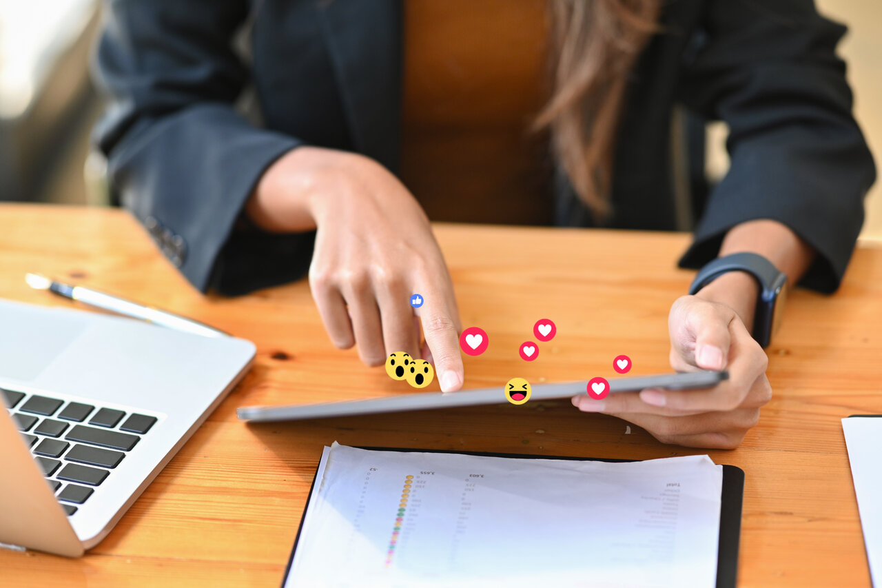 Hand of a woman watching something from a tablet with emojis flying out 